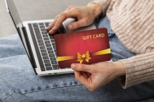 Kvinna som håller i ett gåvokort och väljer produkt på laptop